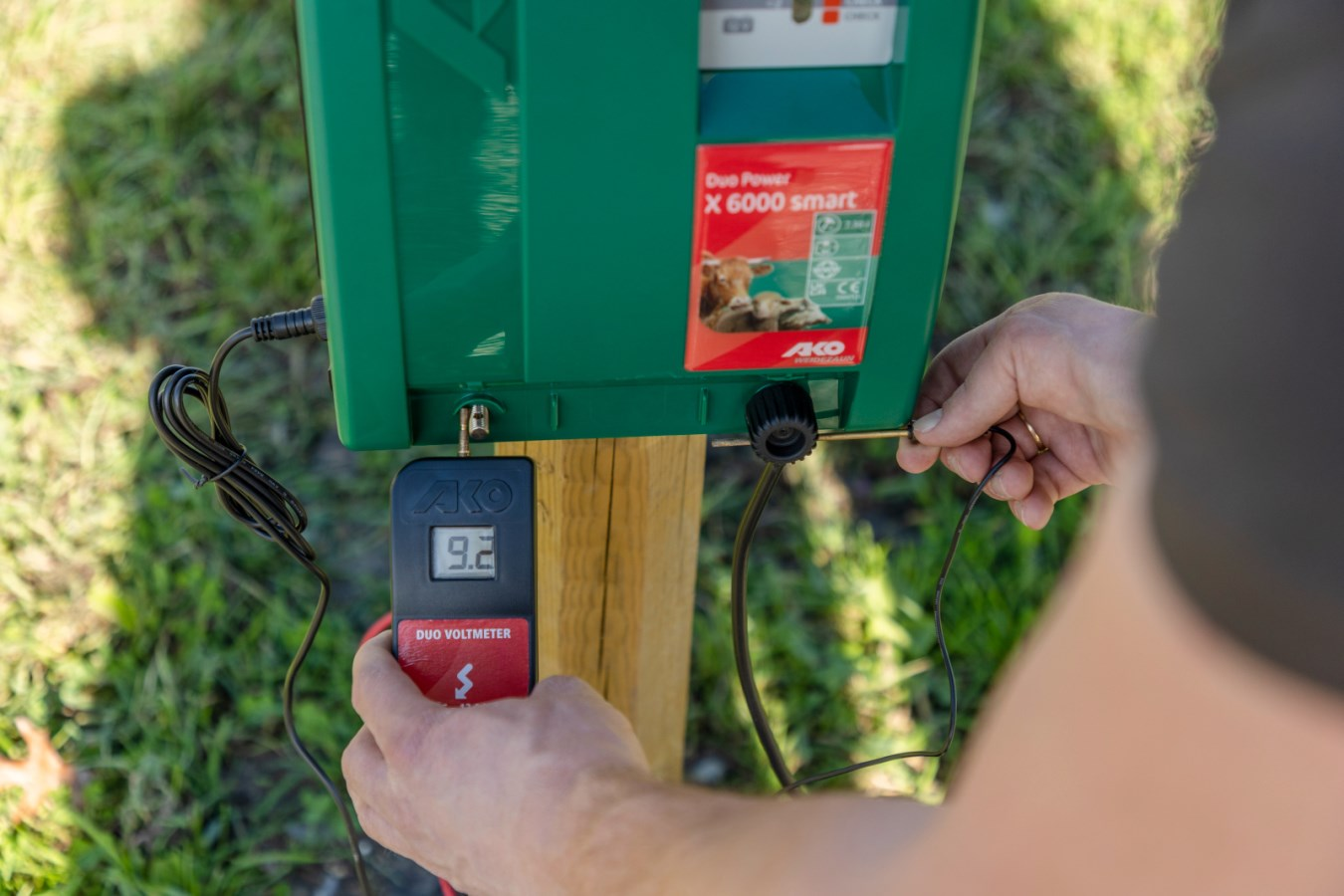 Person misst Spannung eines Weidezaungeräts mit AKO DUO-Voltmeter im Freien