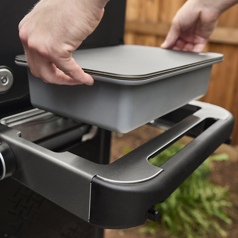 Person schiebt graue Schale in Seitentisch eines Weber SPIRIT EP-325 GBS Gasgrills