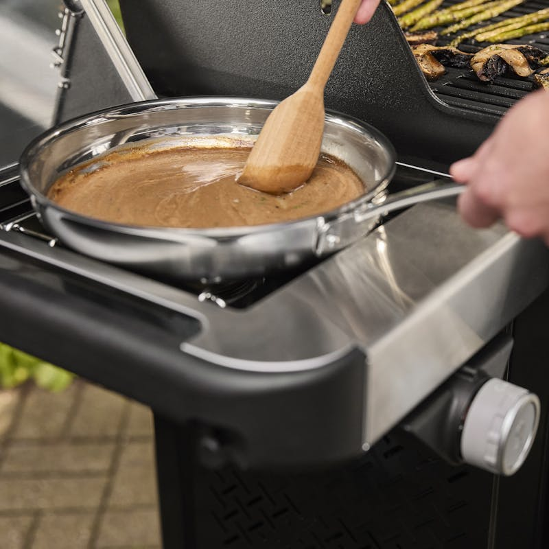 Person verwendet Seitenbrenner des Weber SPIRIT EP-435 GBS Gasgrills zum Zubereiten einer Sauce