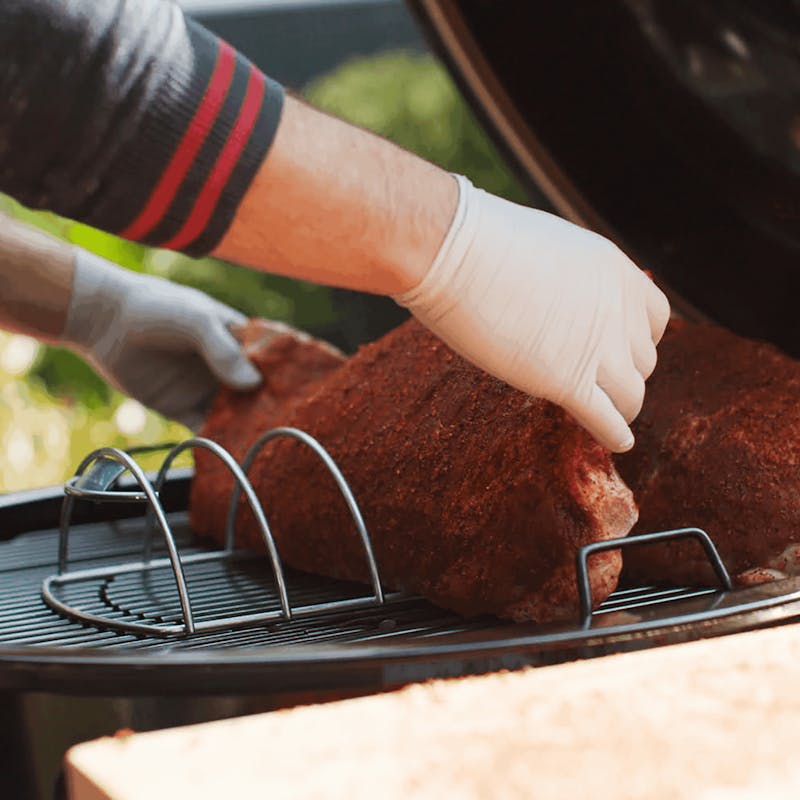 Person platziert Spare-Ribs auf Weber Grillhalter im Freien