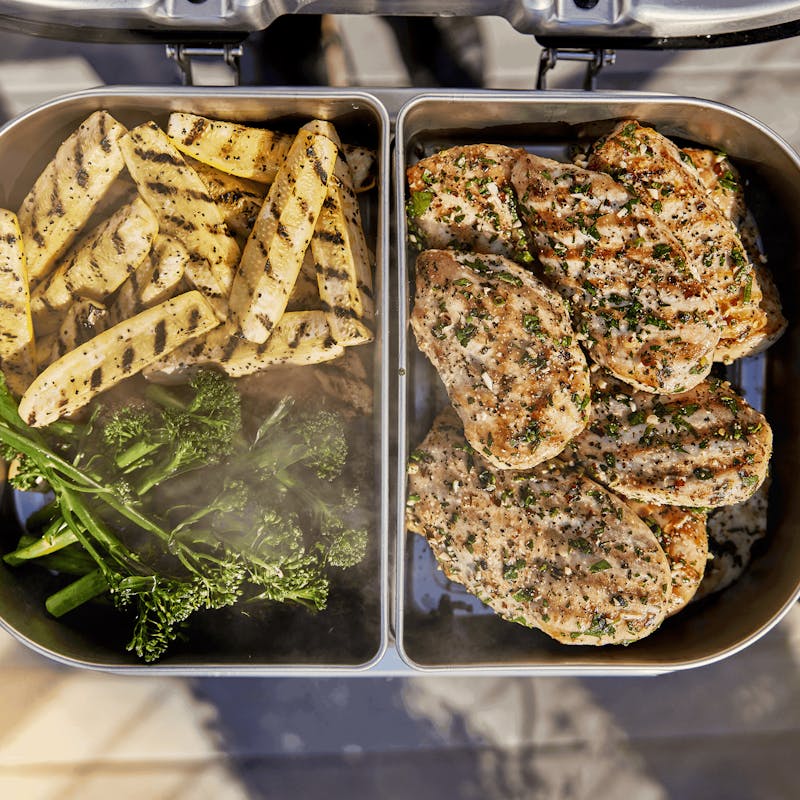 Geöffneter Elektrogrill mit zwei Edelstahlschalen gefüllt mit gegrilltem Gemüse und Hähnchen