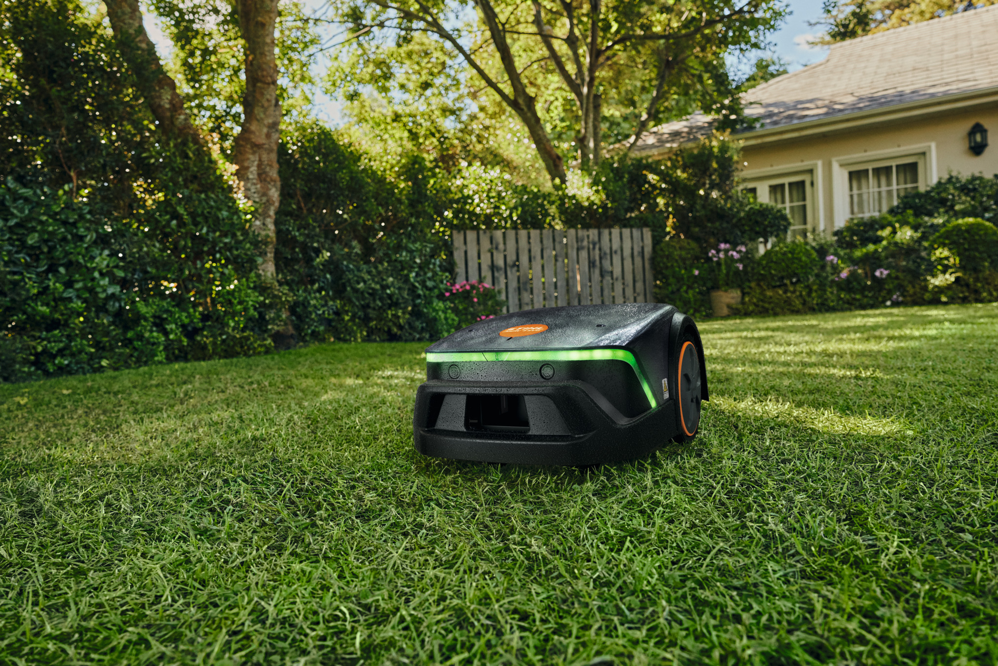 STIHL iMOW 3 EVO Mähroboter mäht Rasen in einem kleinen Garten vor einem Wohnhaus