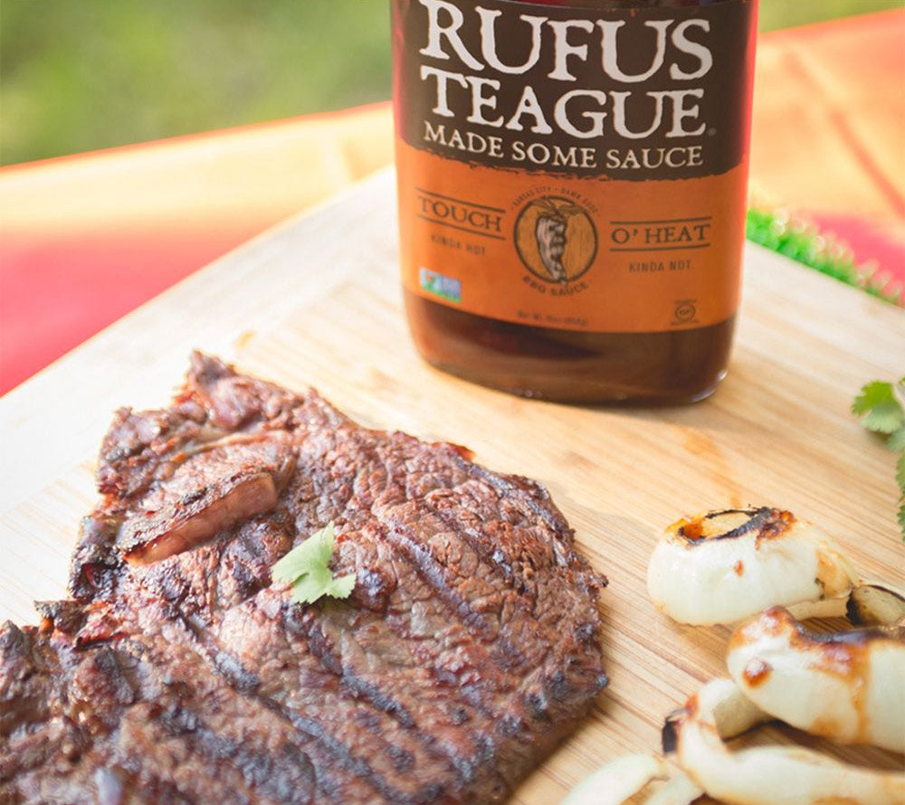 Gegrilltes Steak und Zwiebeln mit Rufus Teague BBQ Sauce auf Holzbrett im Freien