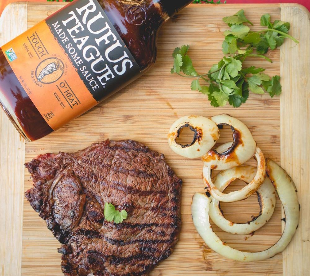 Gegrilltes Steak und Zwiebelringe mit Rufus Teague BBQ Sauce auf Holzbrett