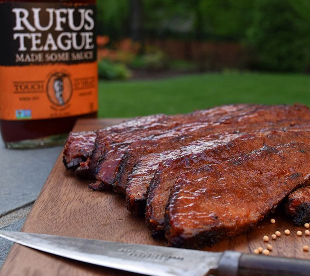 Glasierte BBQ-Rippchen auf Holzbrett mit Rufus Teague Sauce im Garten