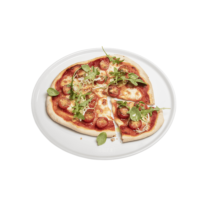 Frische Pizza auf Weber Porzellan-Pizzateller vor grünem Hintergrund