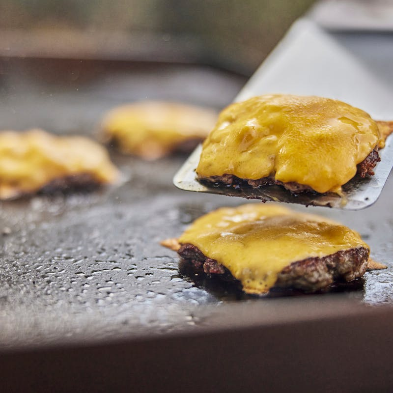 Weber Planchawender hebt Burger mit geschmolzenem Käse auf Grillplatte