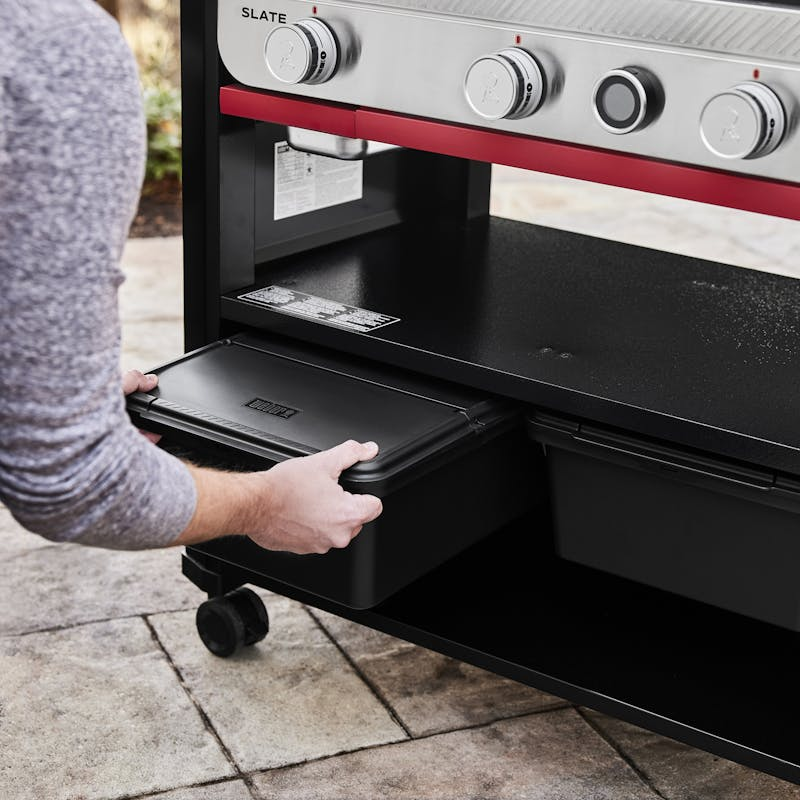 Person zieht schwarze Weber Works Aufbewahrungsbox unter einem Grilltisch hervor