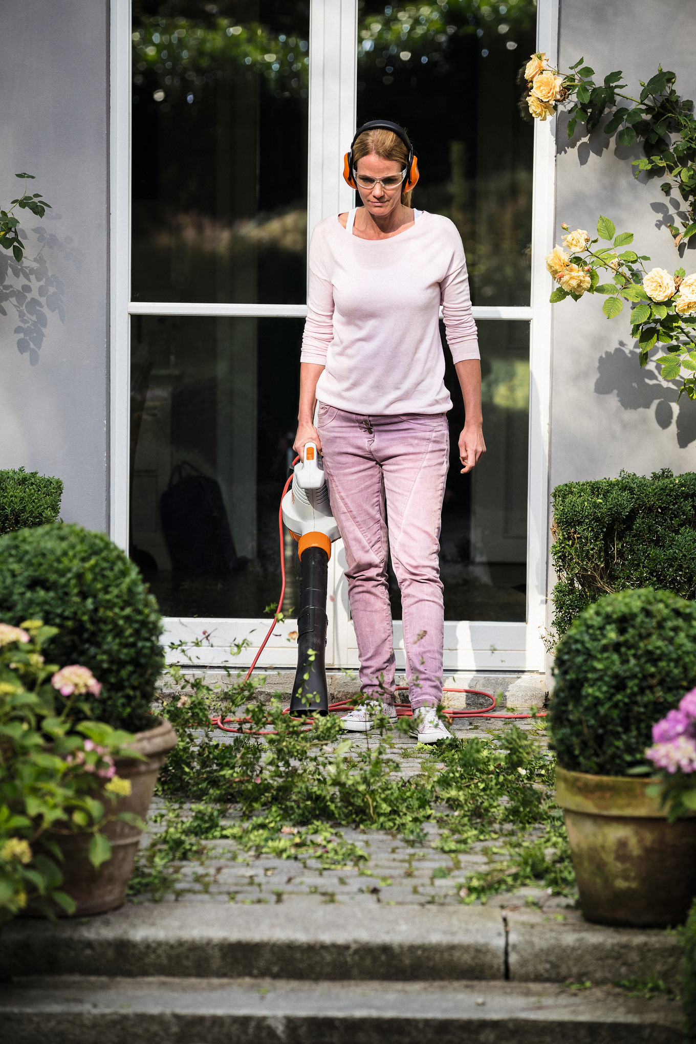 Frau verwendet STIHL BGE 71 Elektro-Laubbläser in einem schönen Garten
