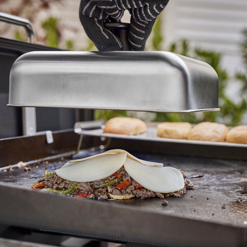 Person verwendet Weber Haube zum Garen von Gemüse und Fleisch auf einer Grillplatte im Freien