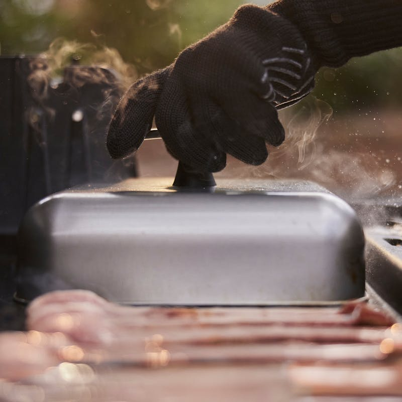Person hebt Weber Haube auf Grill mit Dampf und gegrillten Speisen