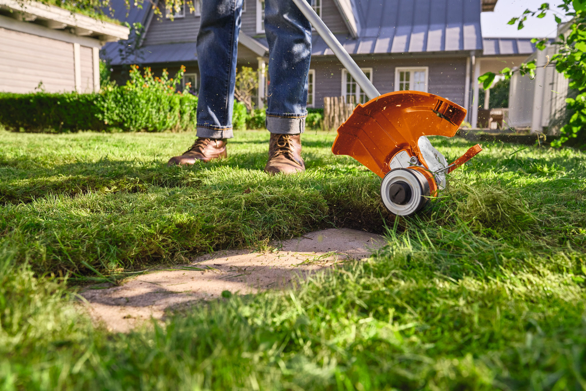 Person verwendet STIHL FSA 50 Akku-Motorsense im sonnigen Garten