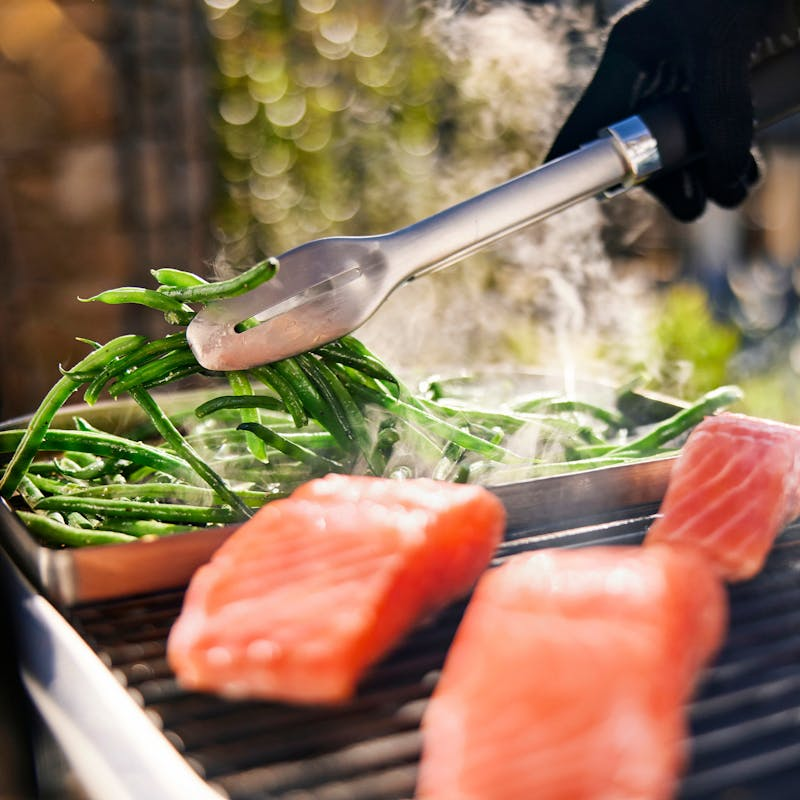Person grillt grüne Bohnen und Lachs auf einem Elektrogrill im Freien