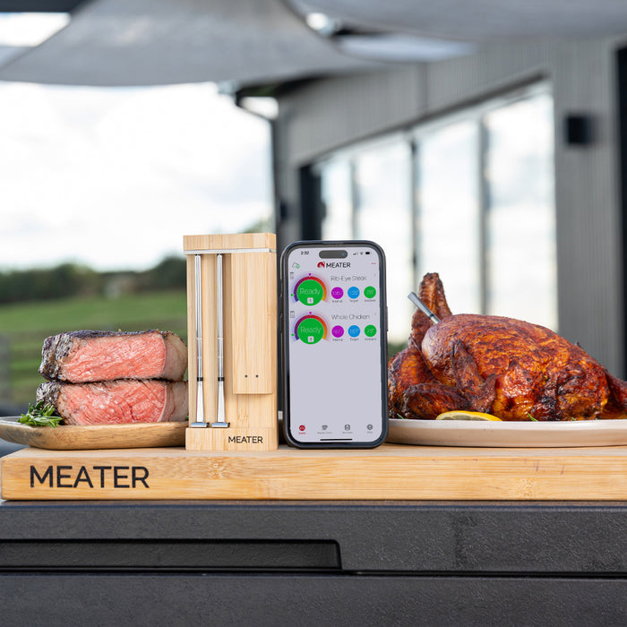 Smartes Fleischthermometer MEATER Pro Duo neben Steak und gebratenem Hähnchen in Außenküche