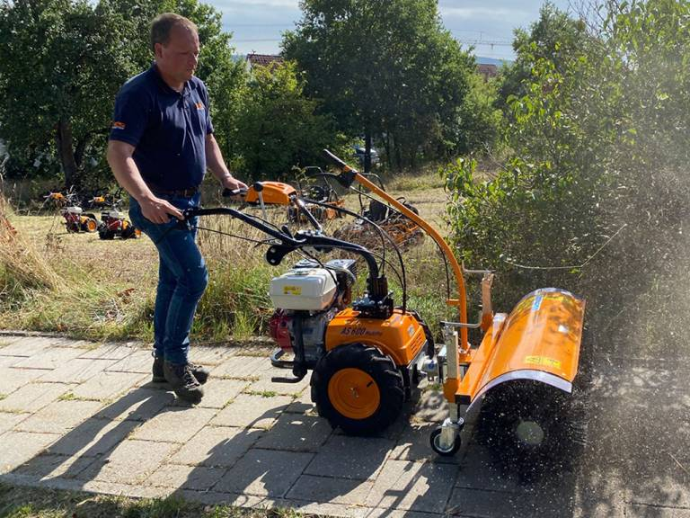 Mann bedient AS 600 MultiPro Mäher mit Honda Motor auf gepflastertem Weg