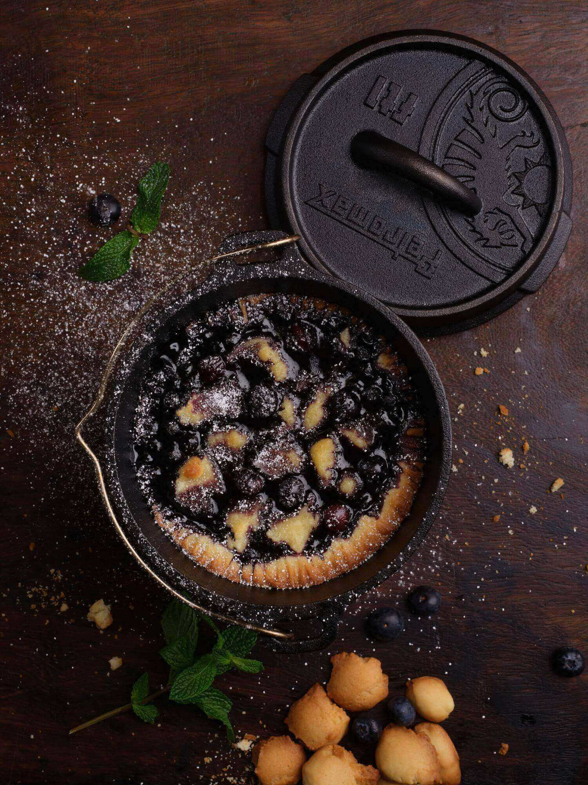 Frischer Blaubeerkuchen im Dutch Oven auf dunklem Holztisch mit Minze und Blaubeeren