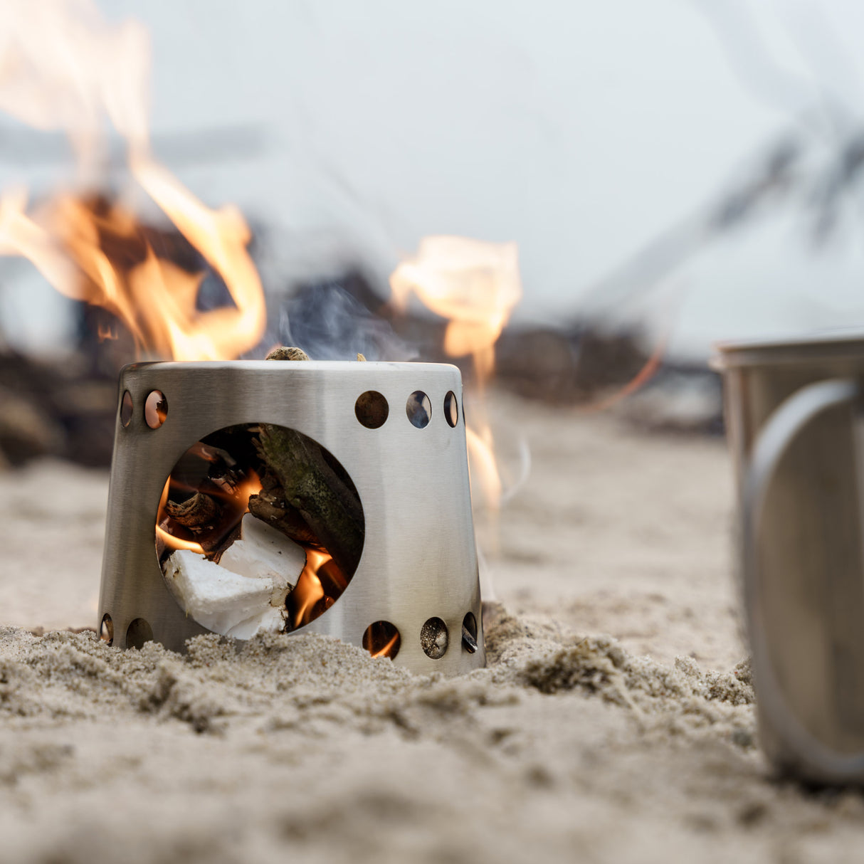 Petromax Kochbecher und Brennstoffbehälter im Einsatz am Strand mit sichtbaren Flammen