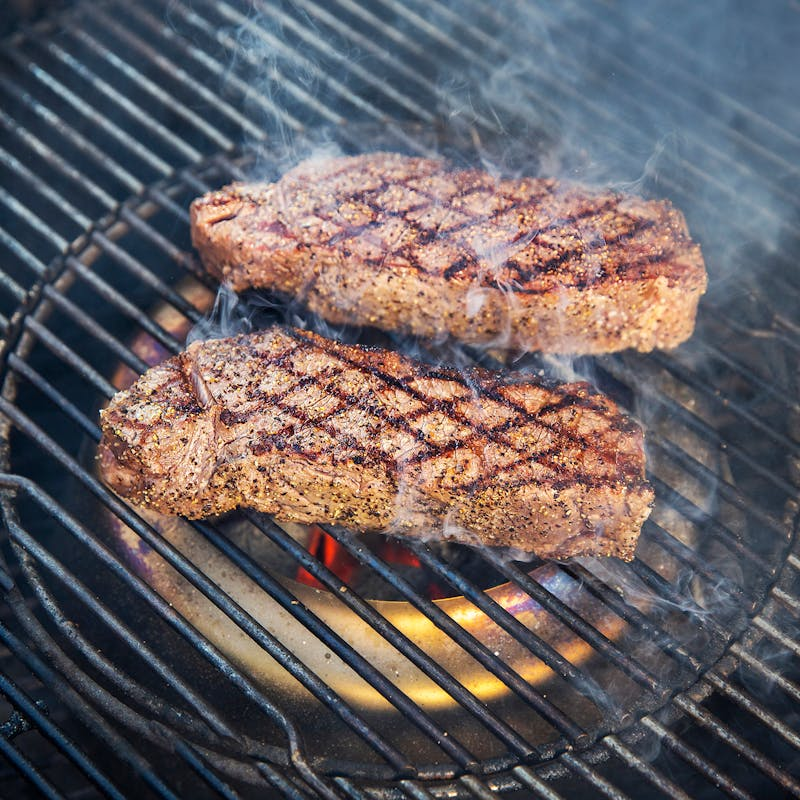 Steaks auf einem Holzkohlegrill mit sichtbarem Diffusorring und glühenden Kohlen