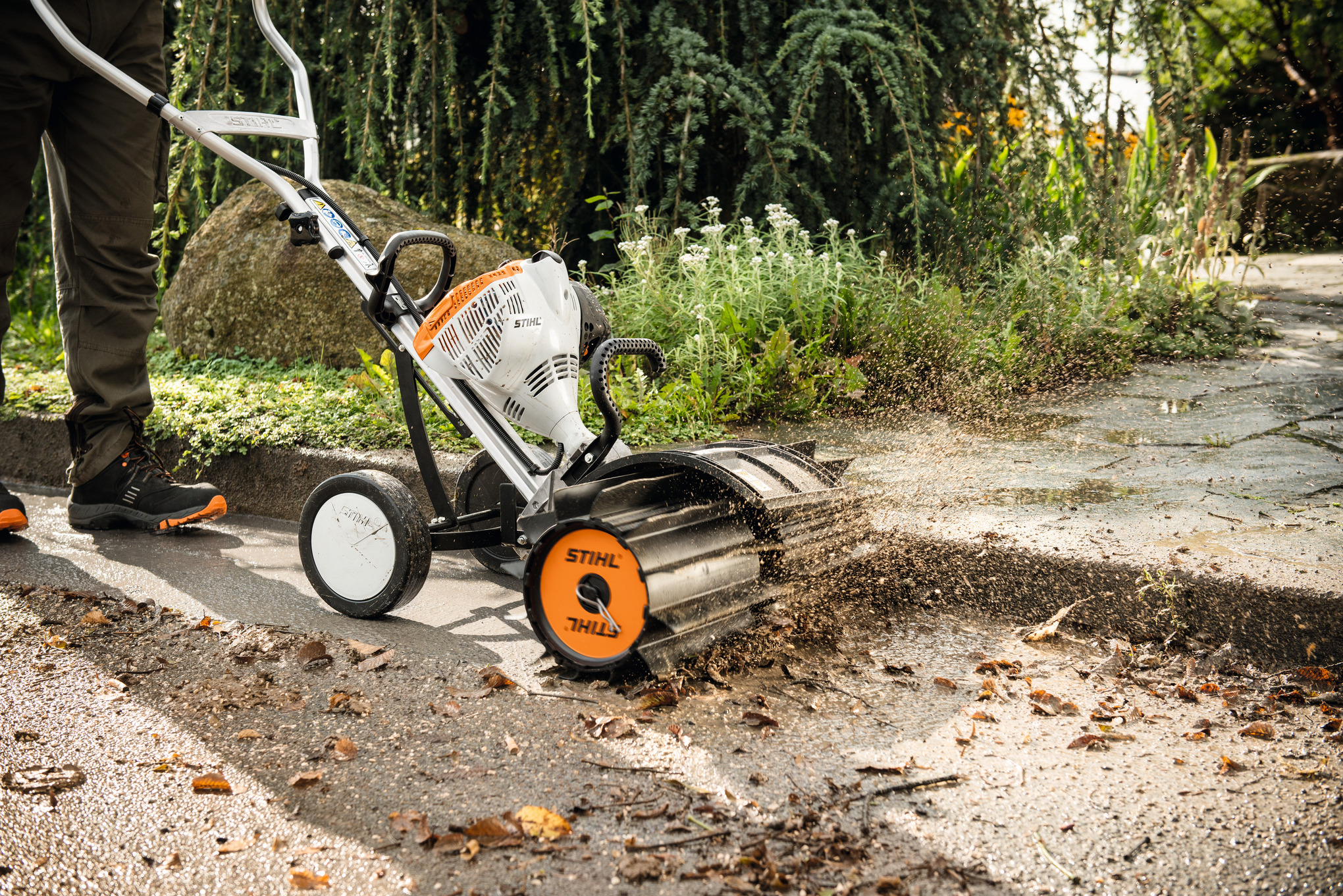 Person verwendet STIHL Kehrwalze zur Reinigung eines Gehwegs