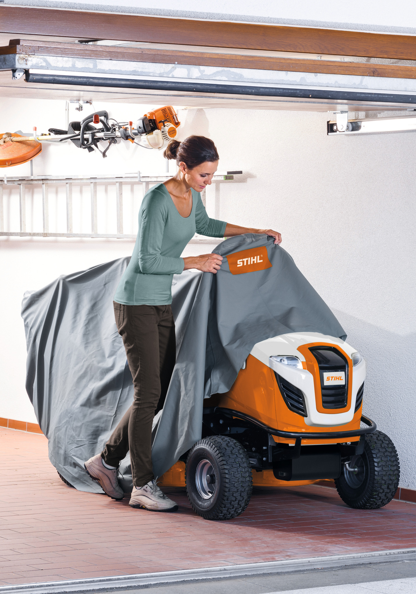 Frau zieht STIHL Abdeckhaube über einen Aufsitzmäher in einer Garage