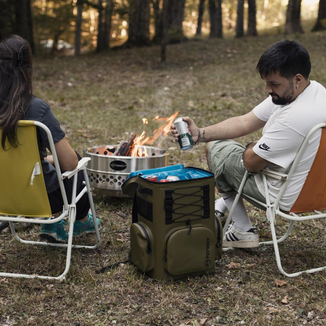 Zwei Personen entspannen am Lagerfeuer mit Petromax Kühlrucksack im Wald