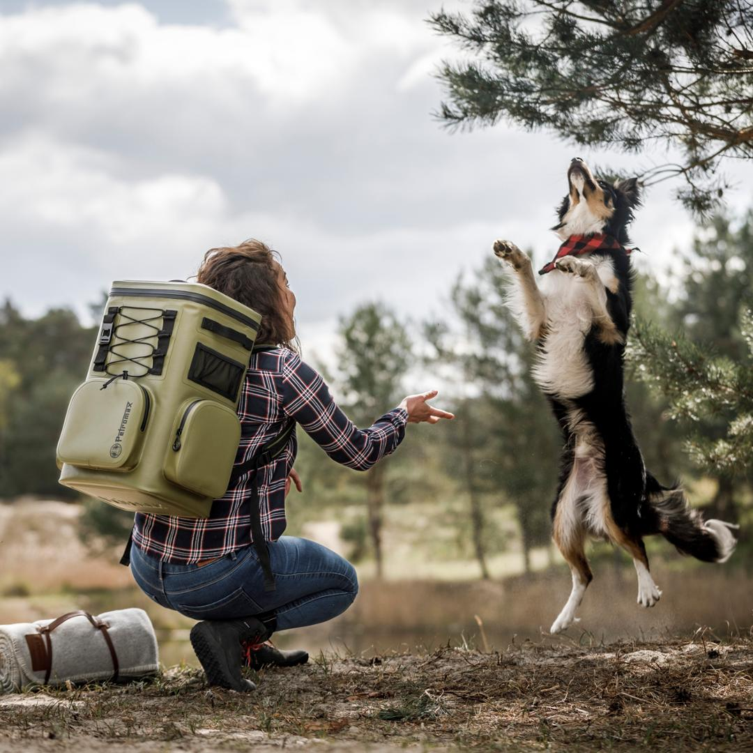 Frau mit Petromax Kühlrucksack spielt mit Hund in der Natur