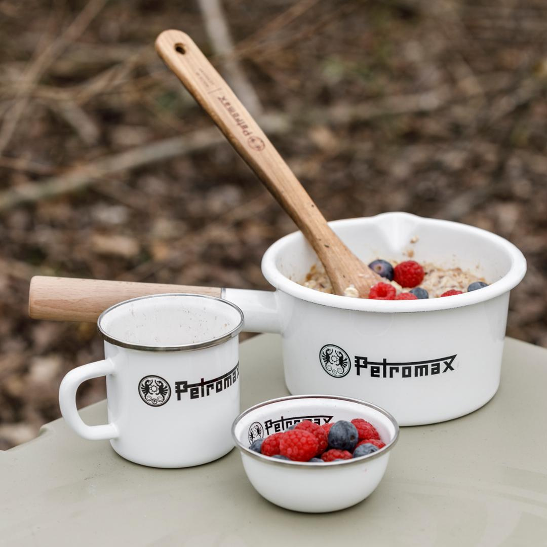 Petromax Holzlöffel in Schüssel mit Müsli und Beeren, umgeben von weiterem Geschirr mit Logo