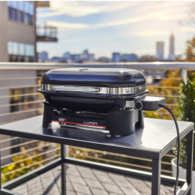 Weber LUMIN COMPACT Elektrogrill auf Terrasse mit städtischer Skyline im Hintergrund