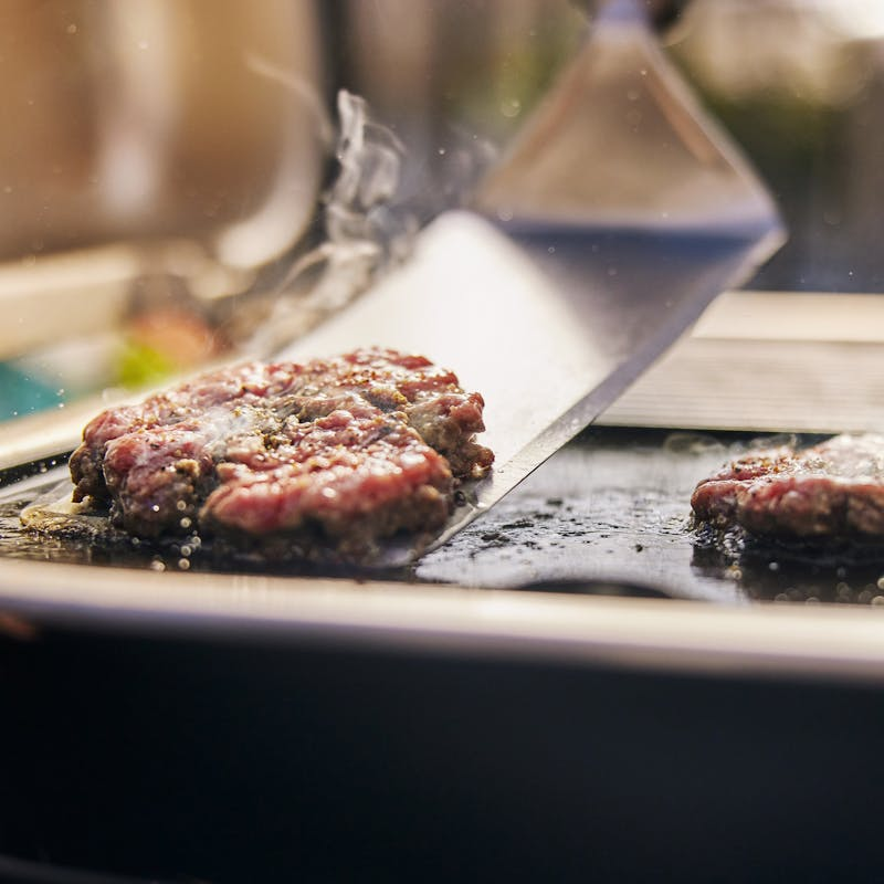 Rinderhacksteaks auf einem Elektrogrill mit sichtbarem Dampf und einem Spatel