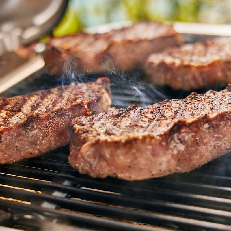 Nahaufnahme von gegrillten Steaks mit Rauch auf einem Grillrost
