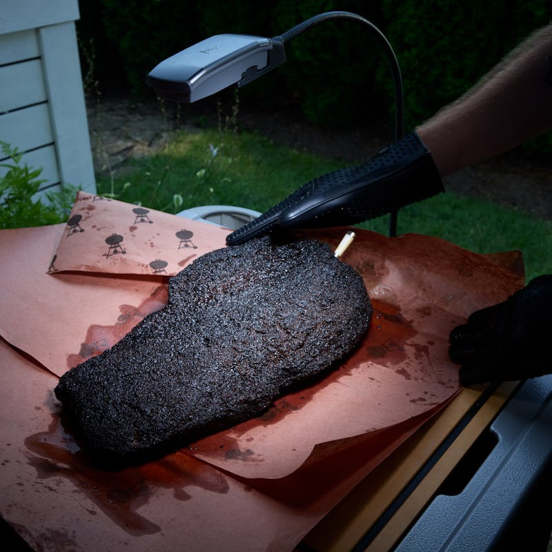 Person checking brisket temperature with digital thermometer on outdoor grill