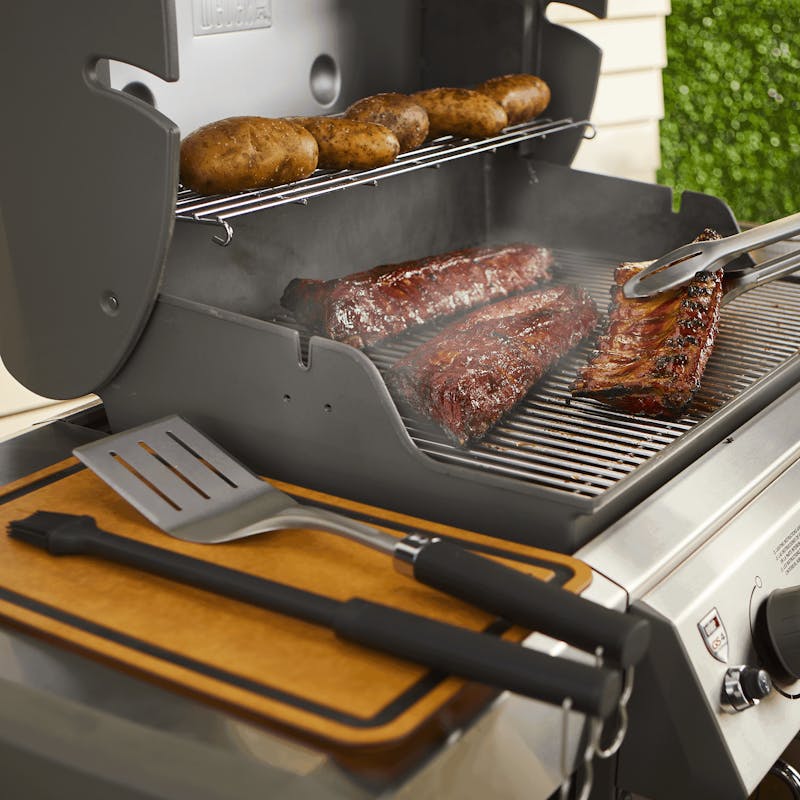 Weber Premium Grillbesteck auf einem Gasgrill mit Steaks und Rippchen im Freien