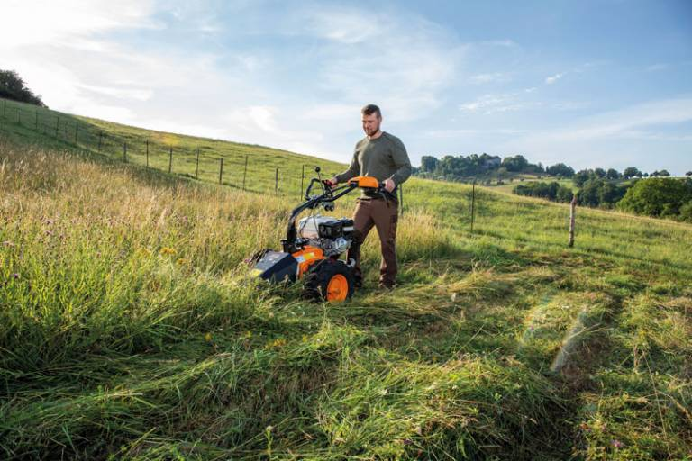 Mann bedient AS LOSI Mähbalken in hügeliger Landschaft