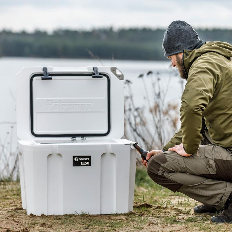 Mann überprüft Petromax Kühlbox mit Schlossplatte am See