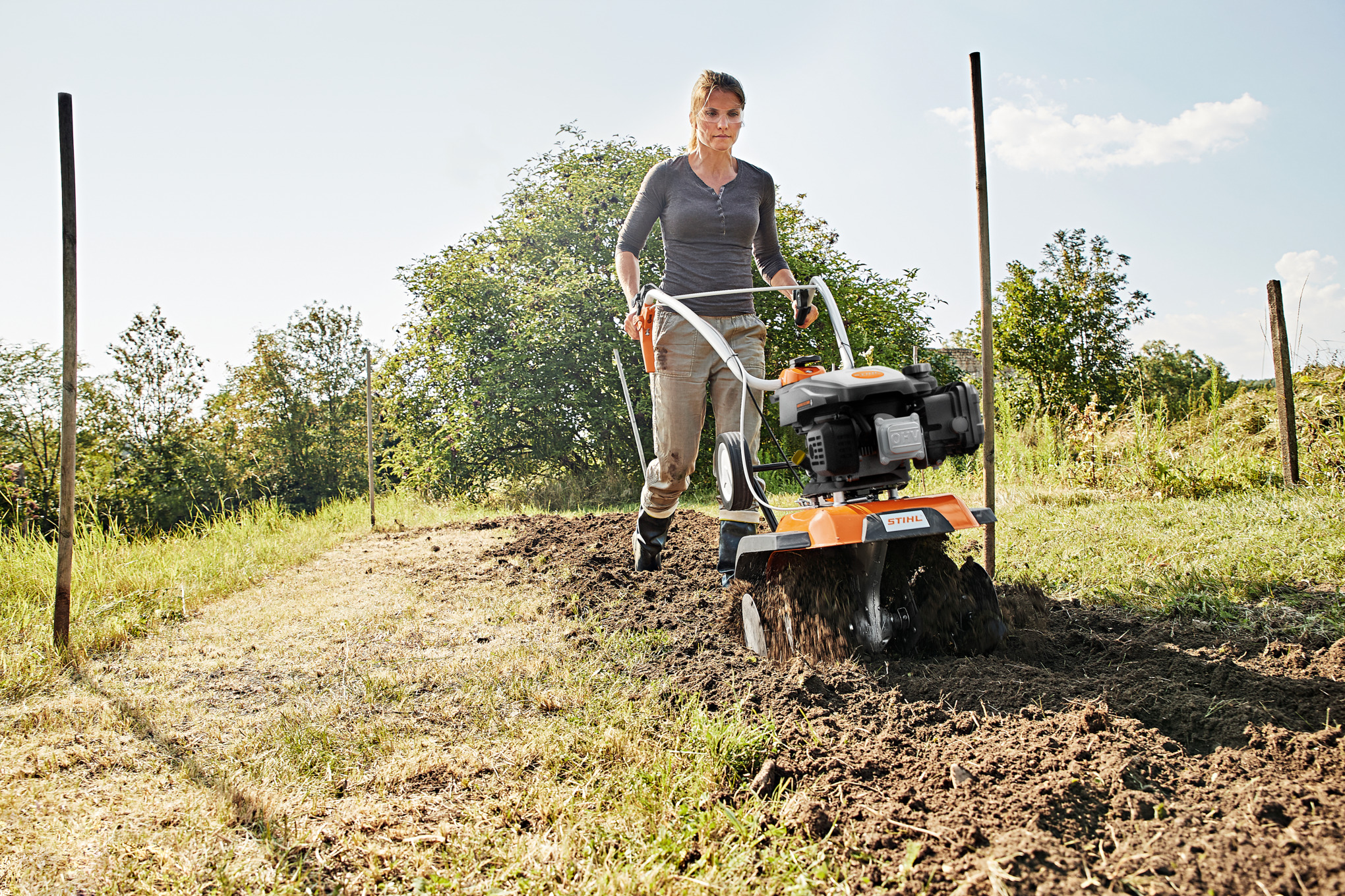 Frau benutzt STIHL MH 445 Motorhacke im Garten bei sonnigem Wetter