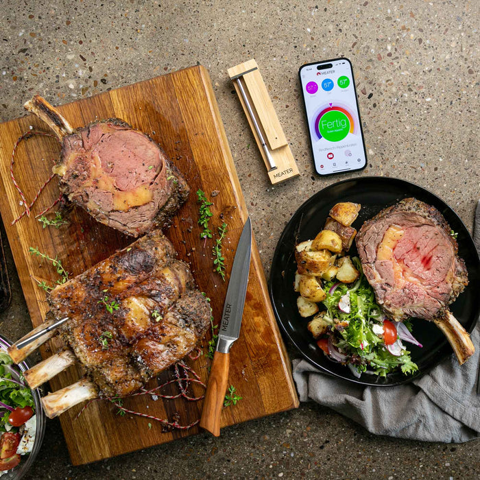 Gebratenes Fleisch auf Holzbrett mit MEATER Pro Thermometer und Smartphone