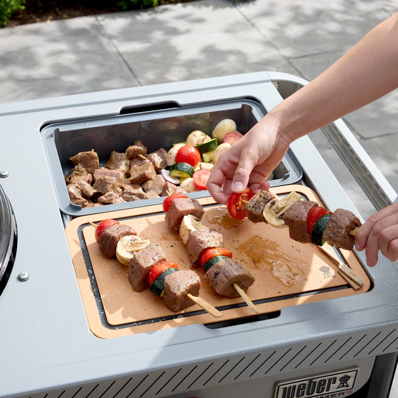Person preparing kebabs on Weber Performer Premium charcoal grill with side table