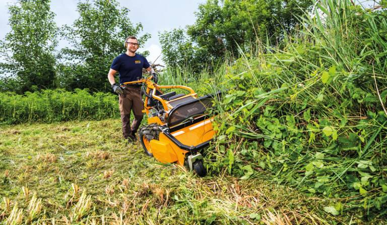 Mann bedient orangefarbenen AS 901 SM Schlegelmulcher auf Wiese