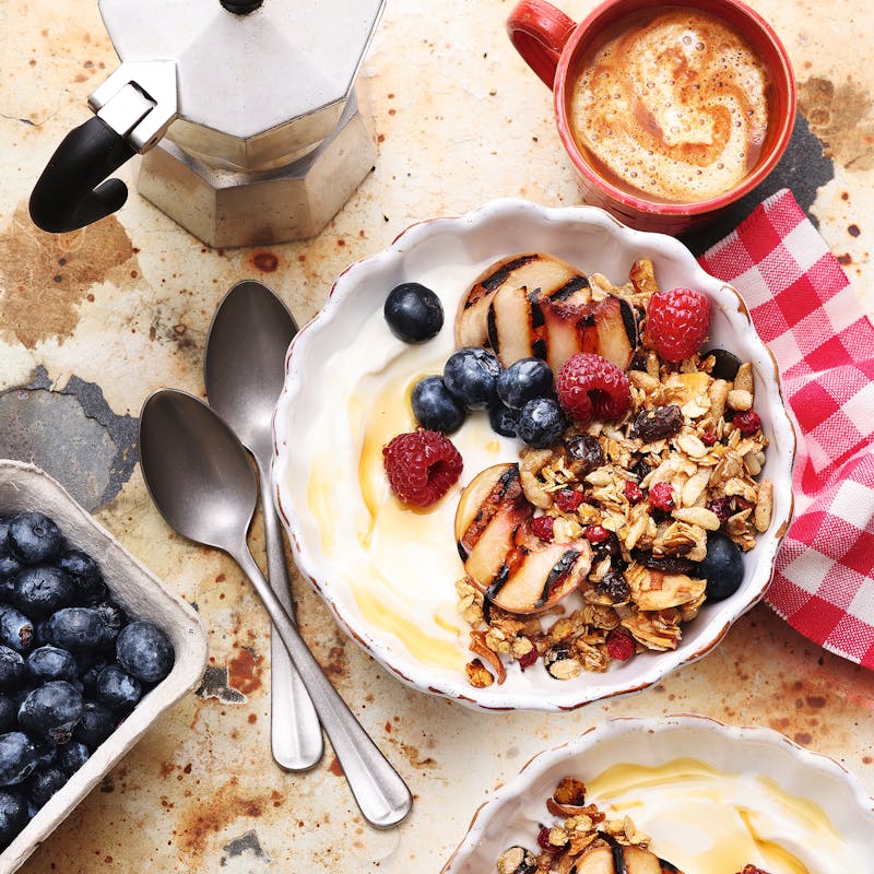 Frühstück mit Joghurt Beeren Nüssen und Kaffee auf rustikalem Tisch