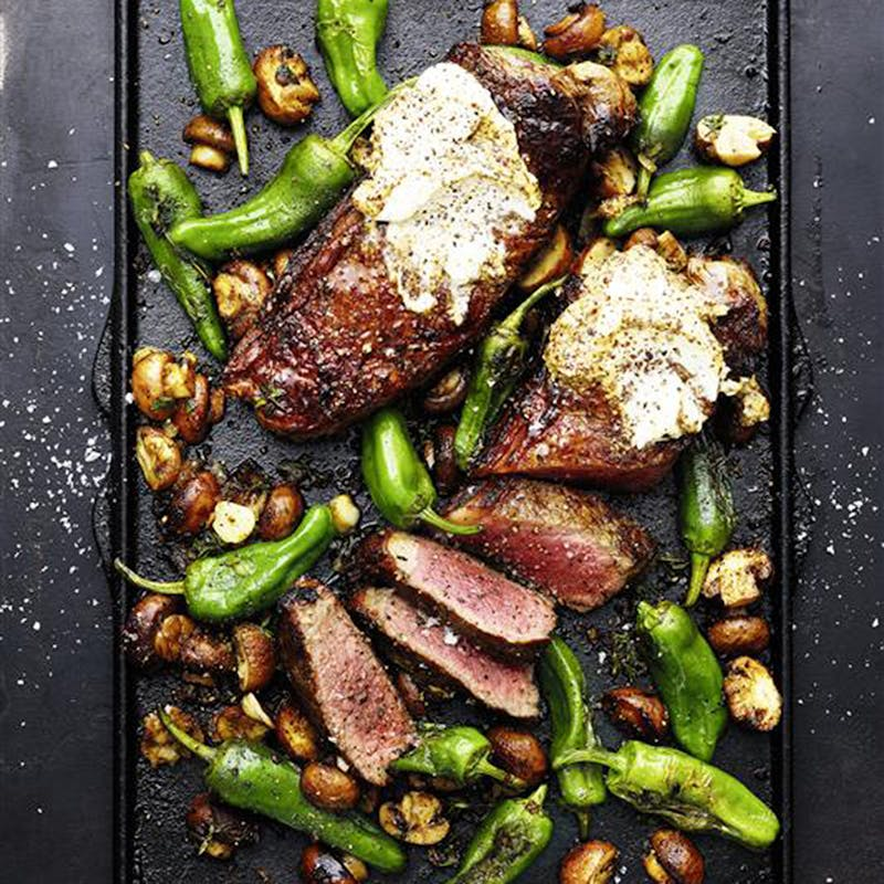 Gegrillte Steaks mit Kräuterbutter und grünen Pfefferoni auf einer Grillplatte
