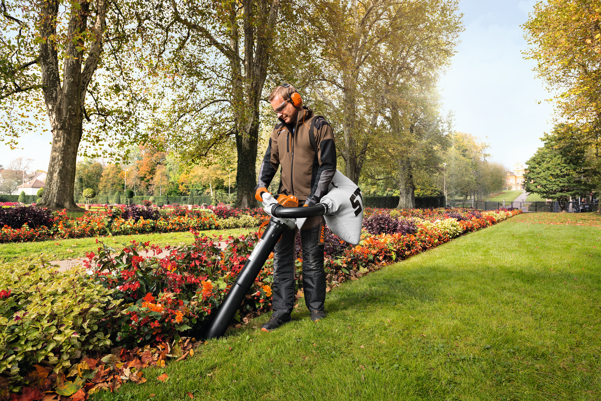 Mann verwendet STIHL SH 86 Saughäcksler in einem blumenreichen Park