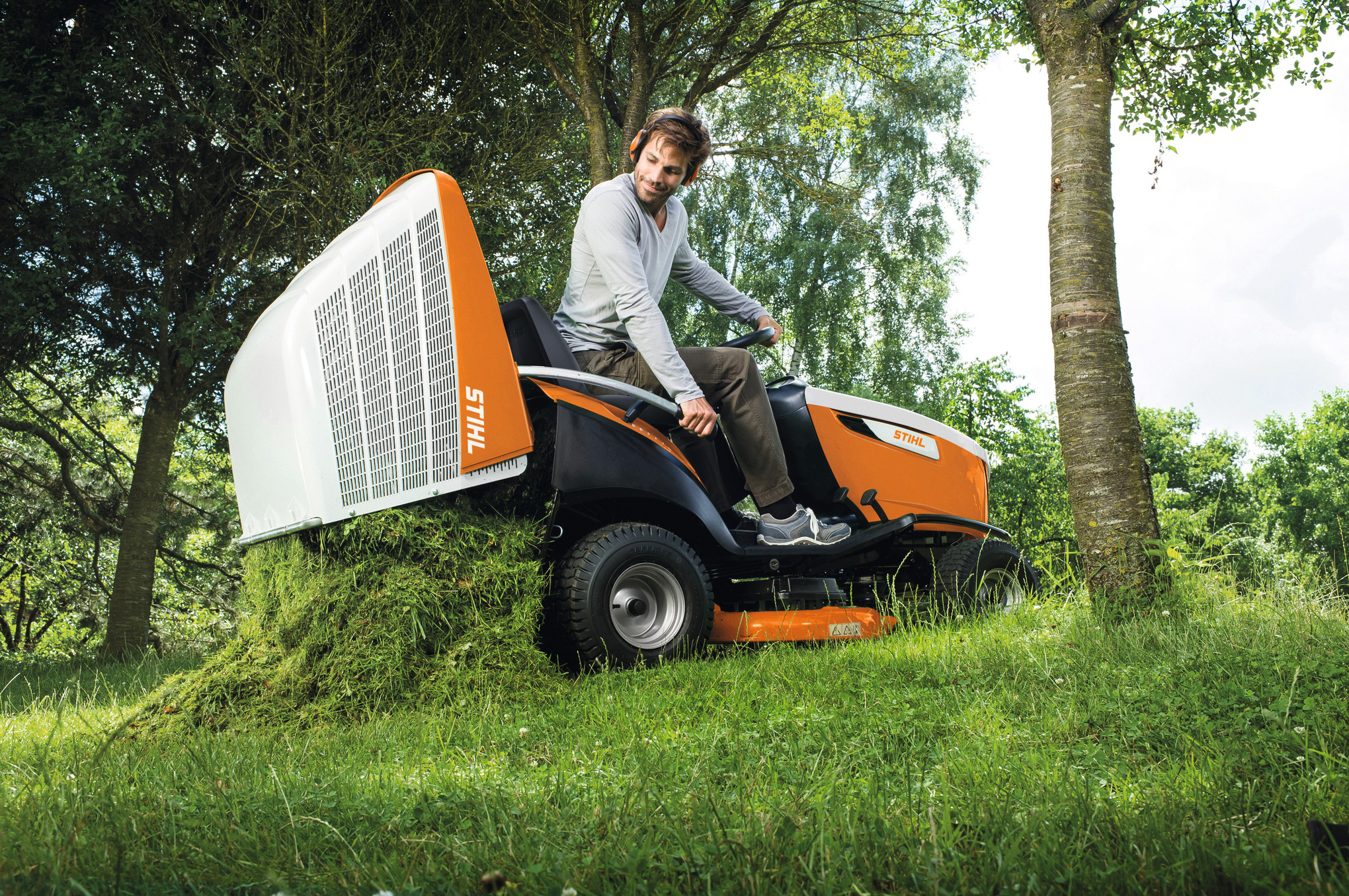 Mann zeigt Grasfangkorb eines STIHL RT 6112 ZL Aufsitzmähers in natürlicher Umgebung