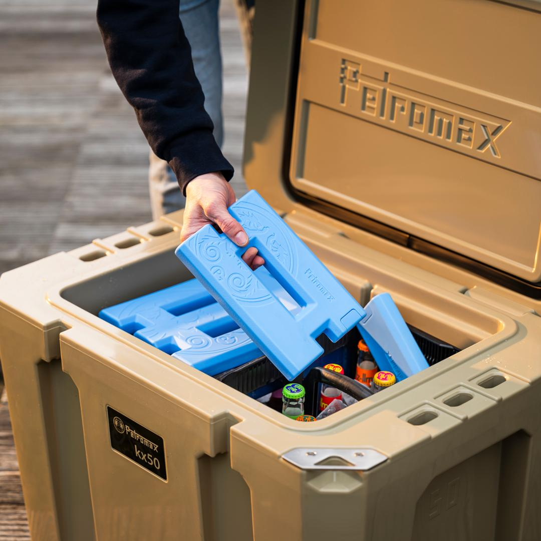 Person legt blaue Kühlakkus in eine Petromax Kühlbox voller Getränke auf einer Holzplattform