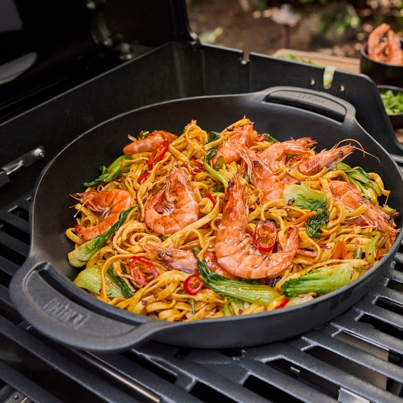 Gebratene Nudeln und Garnelen in einer Grillpfanne auf einem Gasgrill