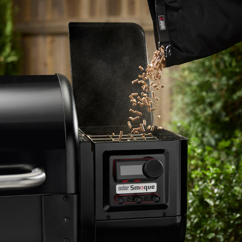 Person füllt Weber SmokeFire Grill mit Kirschholzpellets im Freien