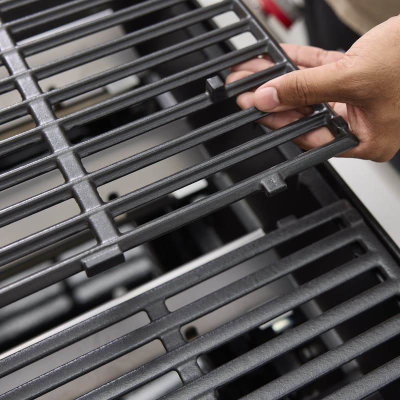Hand hebt einen Gusseisen-Grillrost in einem modernen Gasgrill