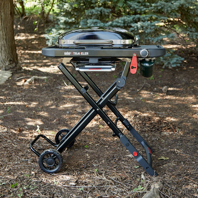 Weber Traveler Compact Gasgrill in einem Wald auf robustem Gestell mit großen Rädern