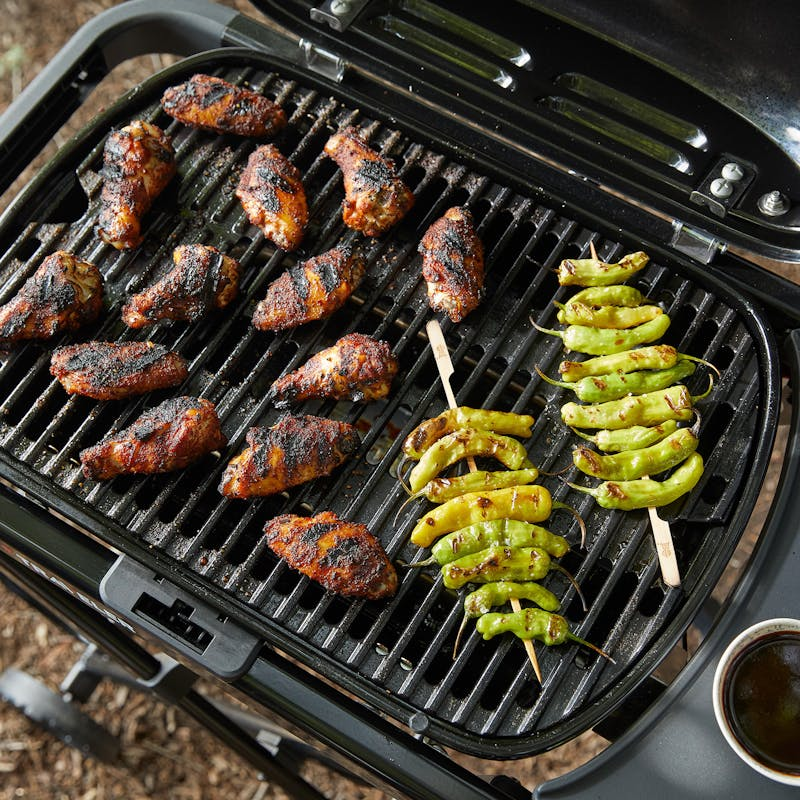 Weber Traveler Compact Gasgrill mit gegrillten Hähnchenteilen und Peperoni in natürlicher Umgebung