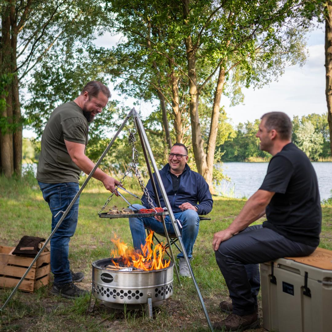 Drei Männer genießen ein Grillfest am See mit einer Petromax Feuerschale Tyropit
