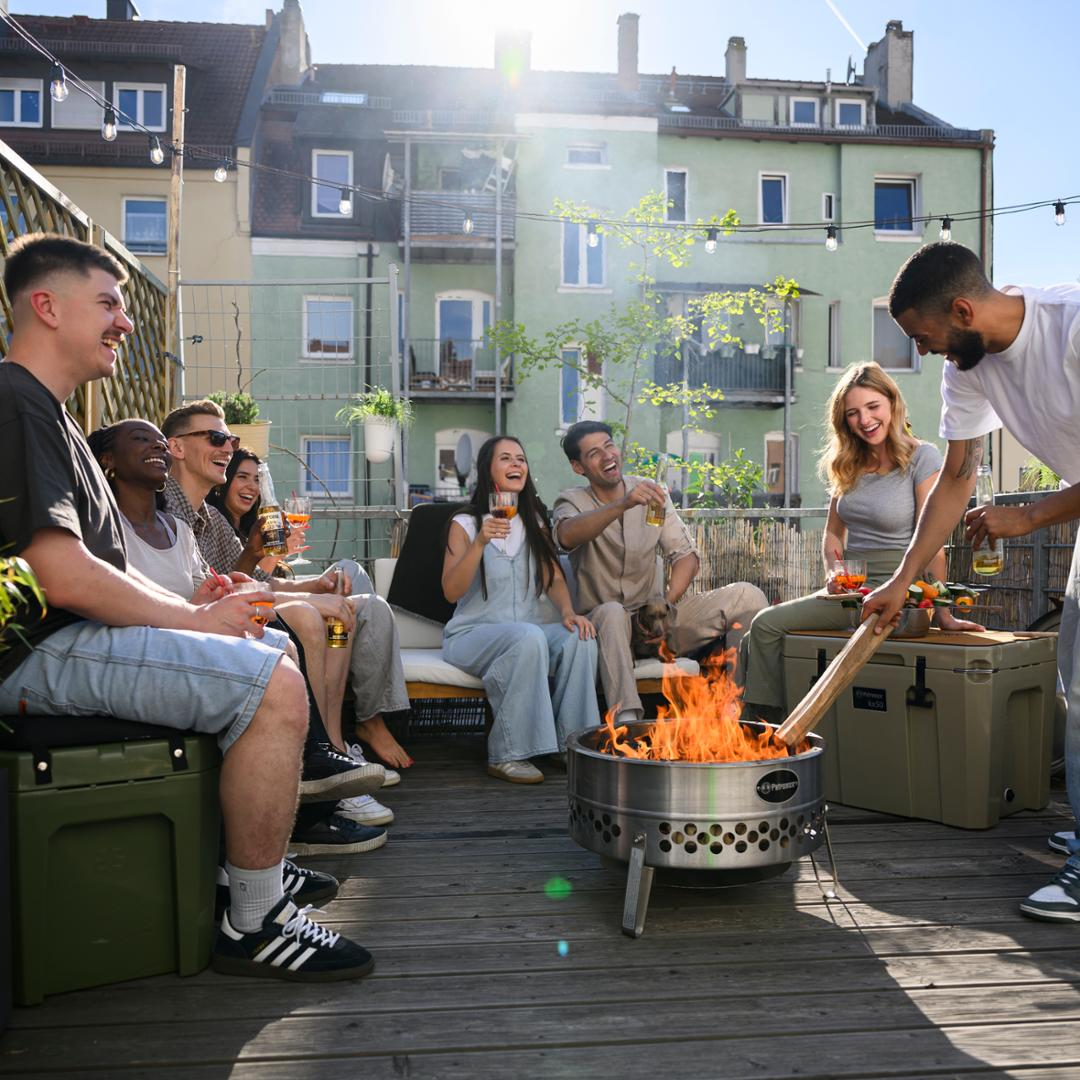 Gruppe junger Erwachsener genießt Zeit um Petromax Feuerschale auf Dachterrasse